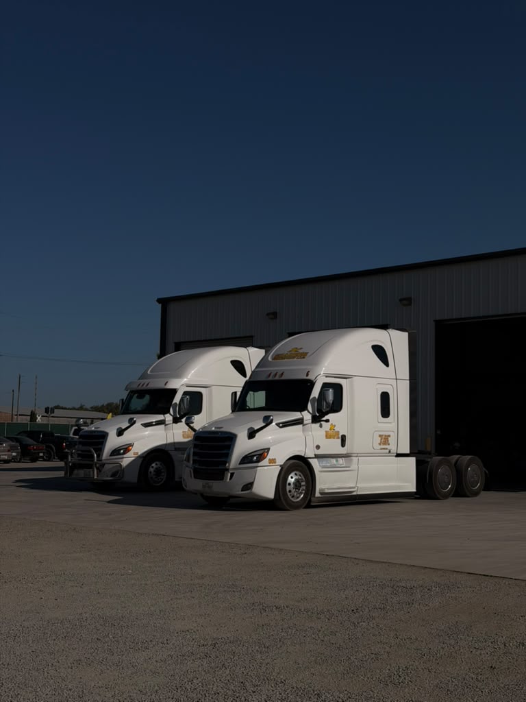 Two Shaheen Transport white tractors parked beside the company building